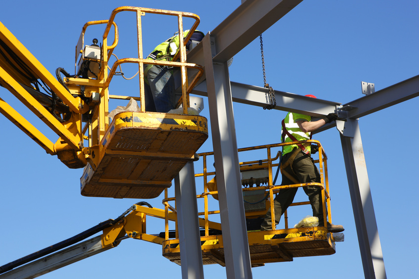 Two steel workers with cherry pickers on a construction site