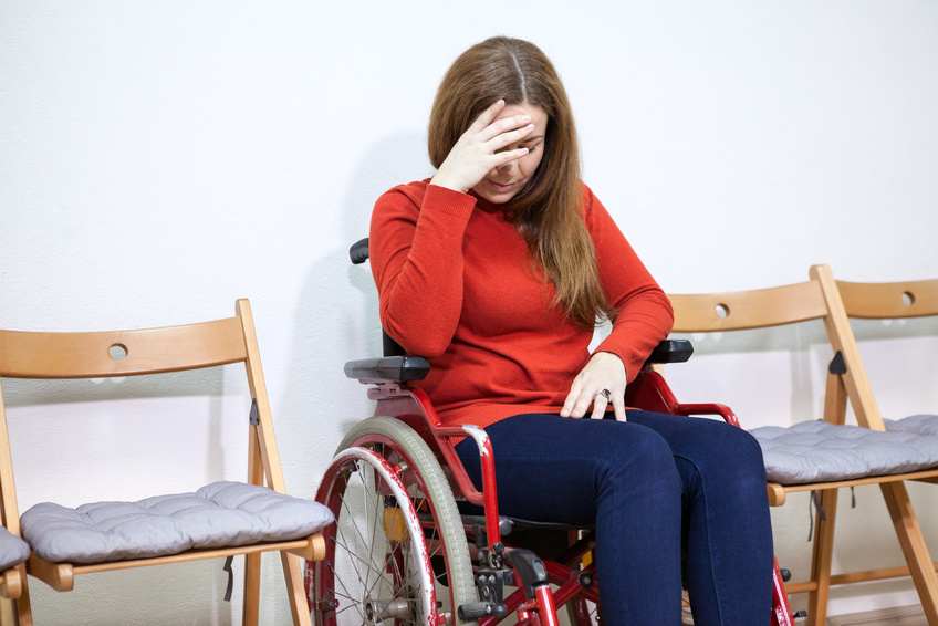 Paralyzed legs sad woman in invalid chair covers her face with hand while sitting between chairs